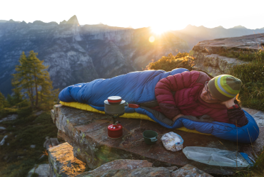 The image showcases an individual sleeping outdoors in nature without a tent, demonstrating bivouacking with minimal equipment specifically for a one-night overnight stay